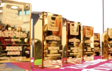 A row of gold trophies sitting on a table covered in fabric with a pull up banner in the background
